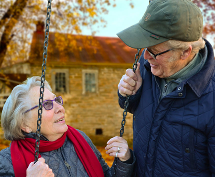 Help Seniors Stay Active - Medicaid or Medicare - Couple enjoy a gaze into each others eyes during autumn she is sitting on a swing he is standing holding the swing chain