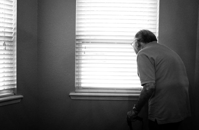 Senior looking out the slit of blinds hanging from the window - recognizing hoarding in the elderly