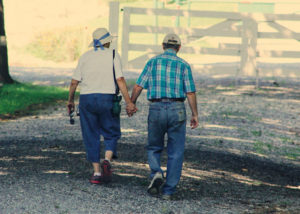 A hiking couple walk in tree shade along a gravel path toward a white gate - aging depression brain fog