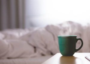 Steaming cup of coffee on the bedside table covers rumpled after a night of good sleep - healthy sleep habits for seniors