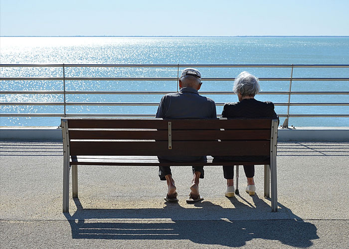 couple sitting on a bench overlooking a sunny ocean - relationships in senior living facility